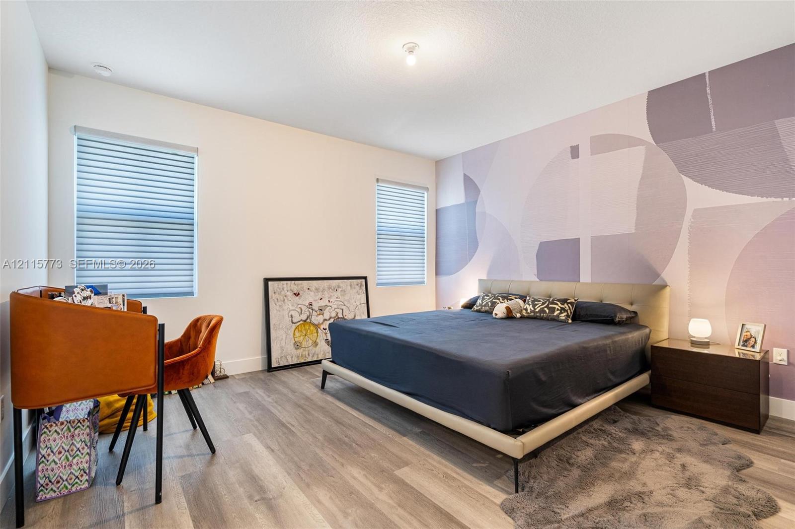 Wood-finish flooring, dual windows with fitted blinds, and a decorative accent wall