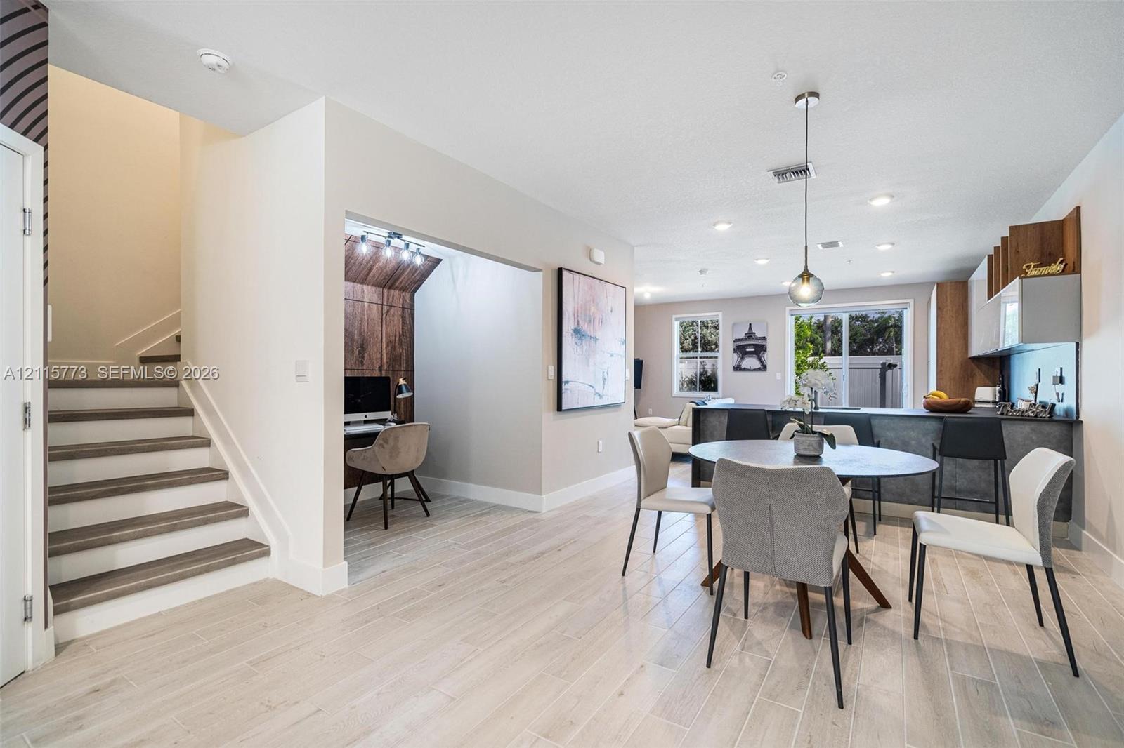 Open-concept interior featuring wood-finish flooring, a built-in wood-accented workspace, recessed lighting, and a kitchen island with stone-surface detailing