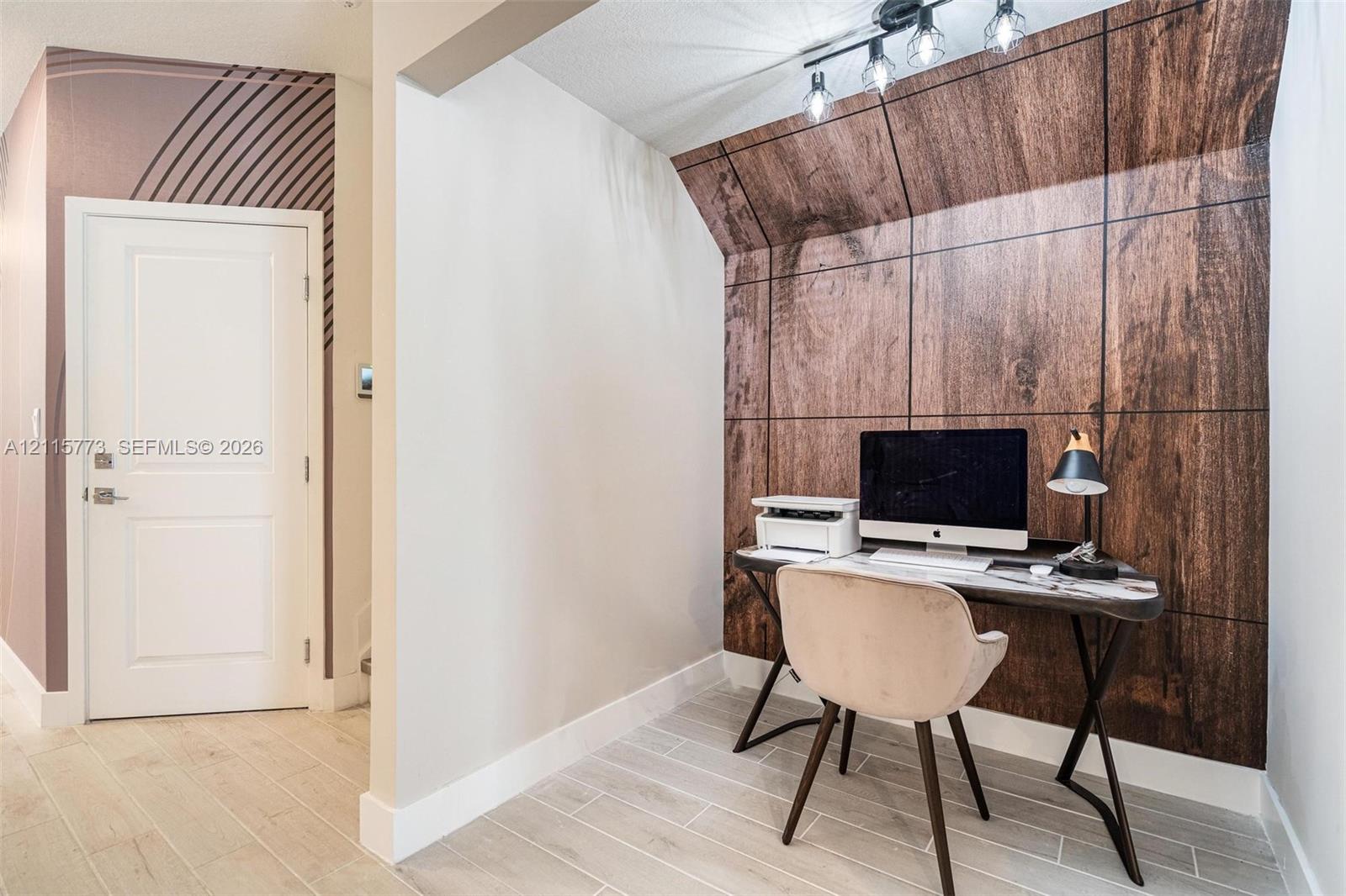 Alcove featuring wood-paneled accent wall, light-toned wood-finish flooring, custom geometric mural, and track lighting
