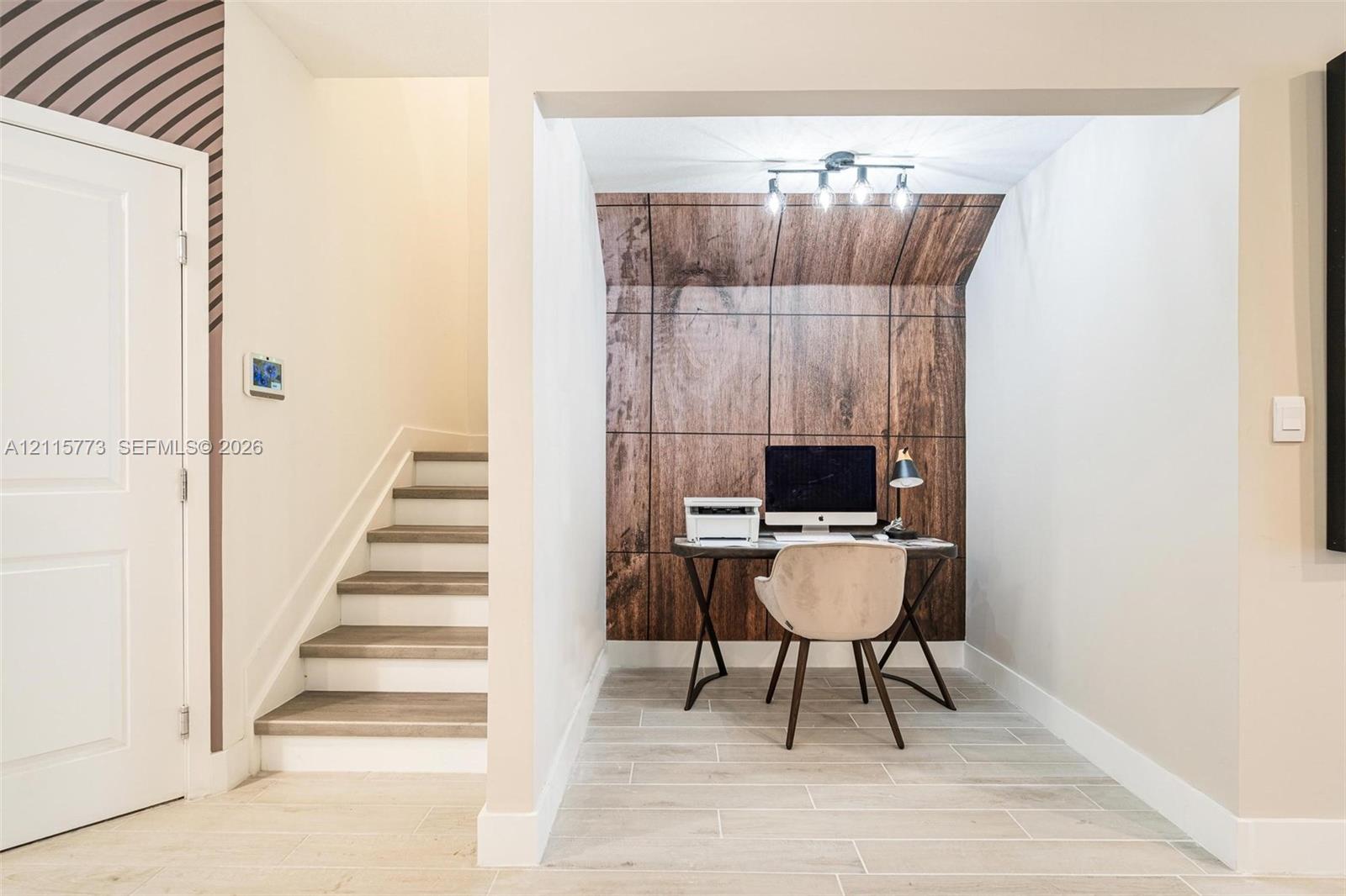 Recessed alcove featuring wood-panel accent wall, tile flooring, and multi-bulb track lighting, positioned near a staircase with wood-finish steps