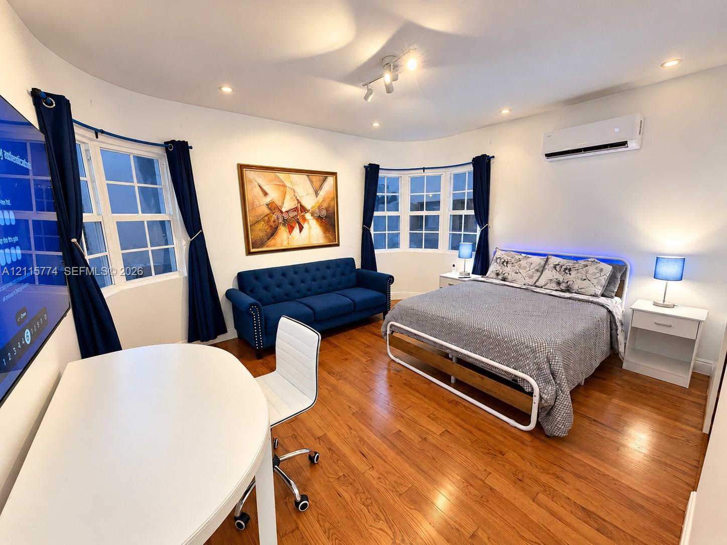 Room featuring wood-finish flooring, two large bay window sets with divided-light panes, recessed lighting, and a wall-mounted ductless climate control unit
