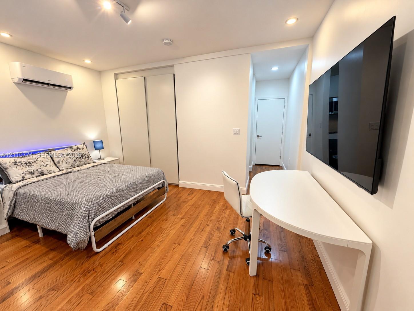 Wood-finish flooring, recessed ceiling lighting, wall-mounted air conditioning unit, and built-in closet with sliding doors