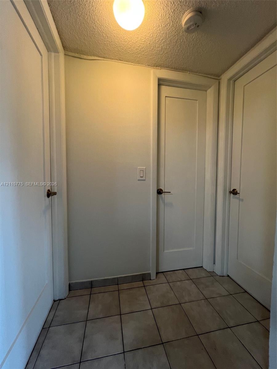 Interior space featuring square ceramic tile flooring, three solid-core shaker-style doors with metallic hardware, and a flush-mount ceiling light fixture