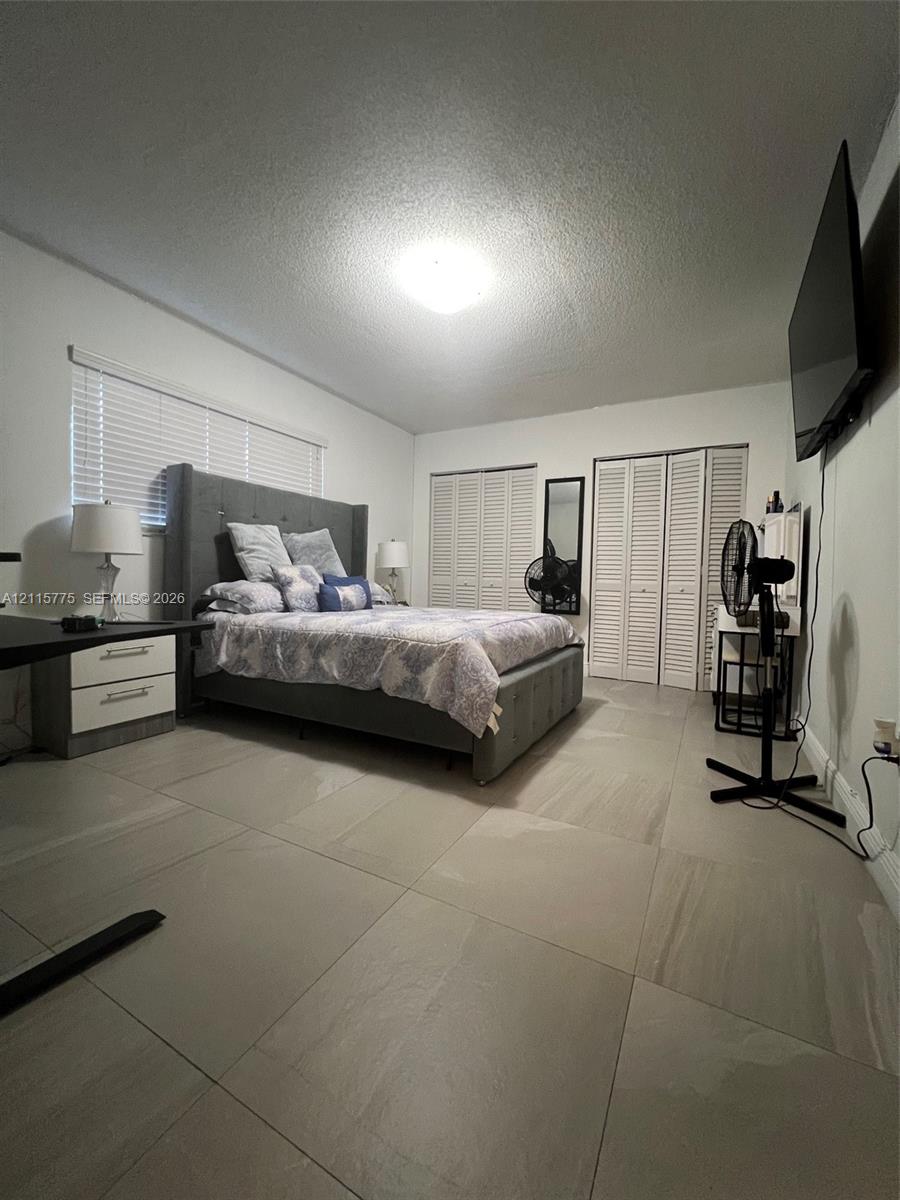 Large-format neutral floor tiling, louvered bi-fold closet doors, and horizontal slat window blinds