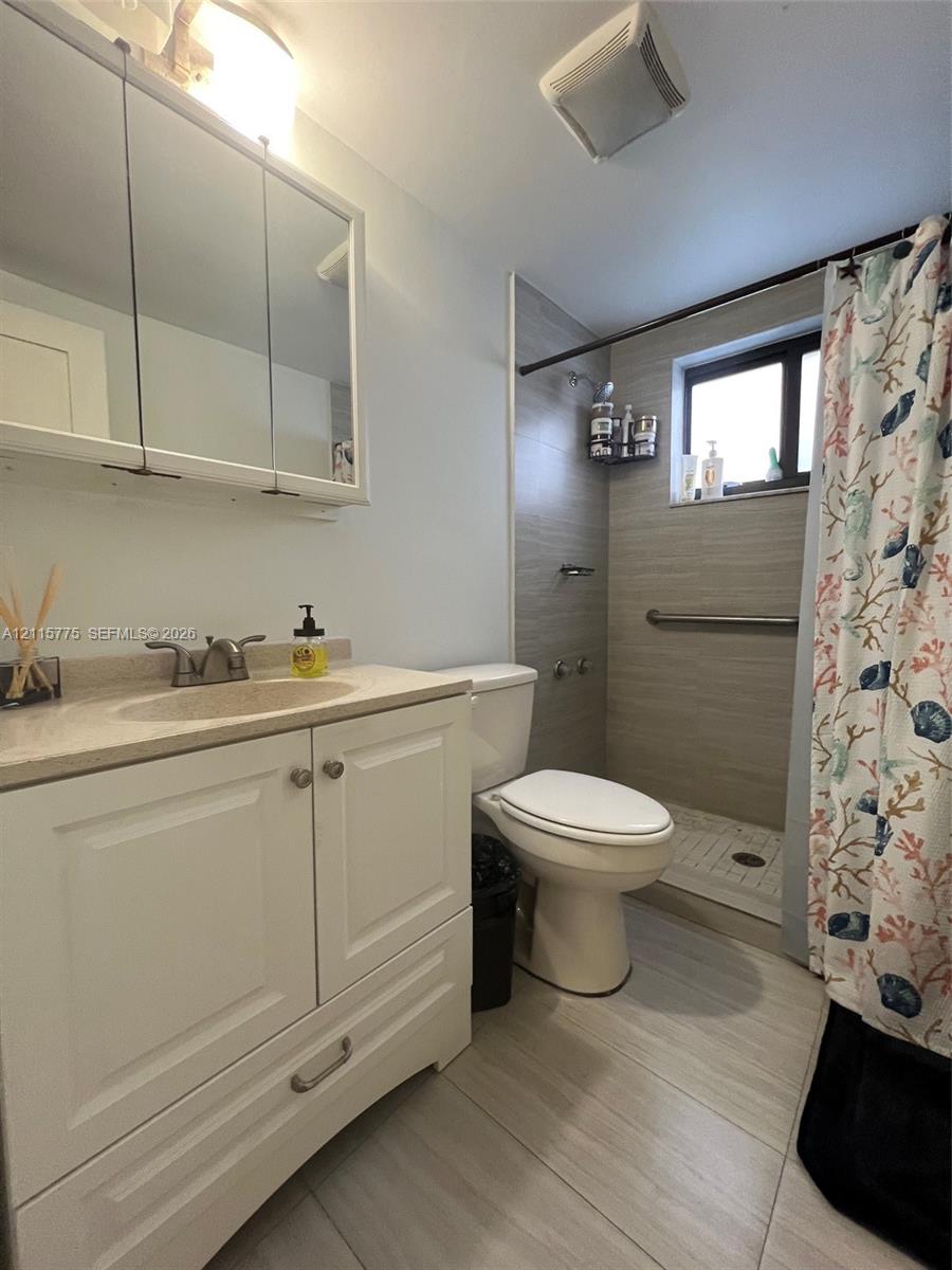 White cabinetry with integrated vanity top and undermount sink, mirrored medicine cabinet, neutral large-format floor tiling, and walk-in shower featuring horizontal tile surround and metal grab bar