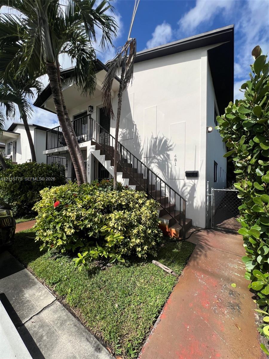 Two-story exterior featuring smooth stucco siding, black metal railings, an open-air staircase, and a concrete walkway