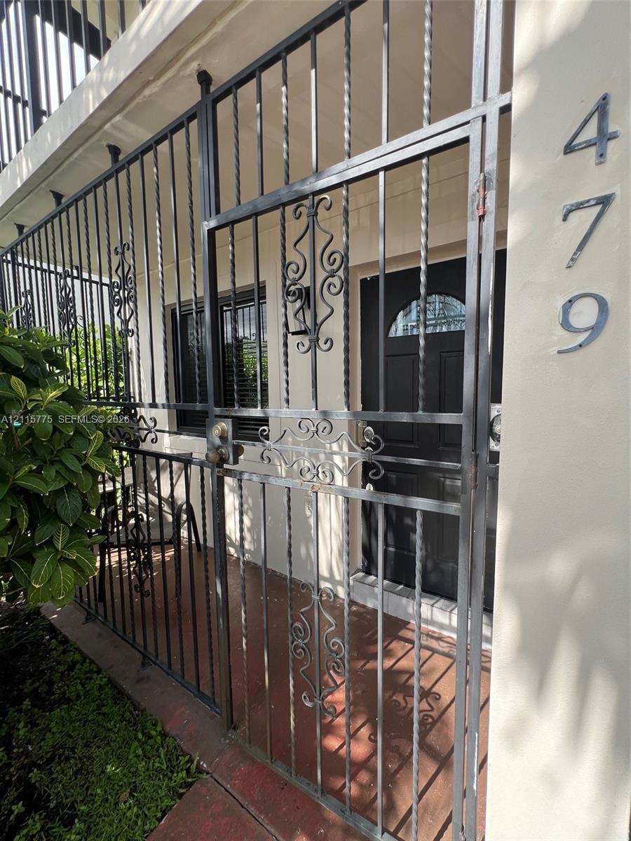 Exterior entryway featuring a black metal security gate with scrollwork detailing, a solid-panel door with a semi-circular glass insert, and mounted house numbers