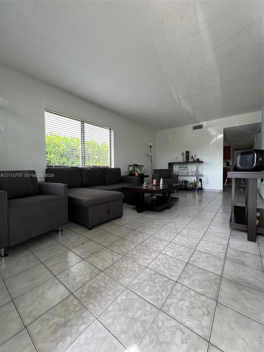 Living area featuring large-format tile flooring, neutral wall paint, and a wide window with integrated blinds