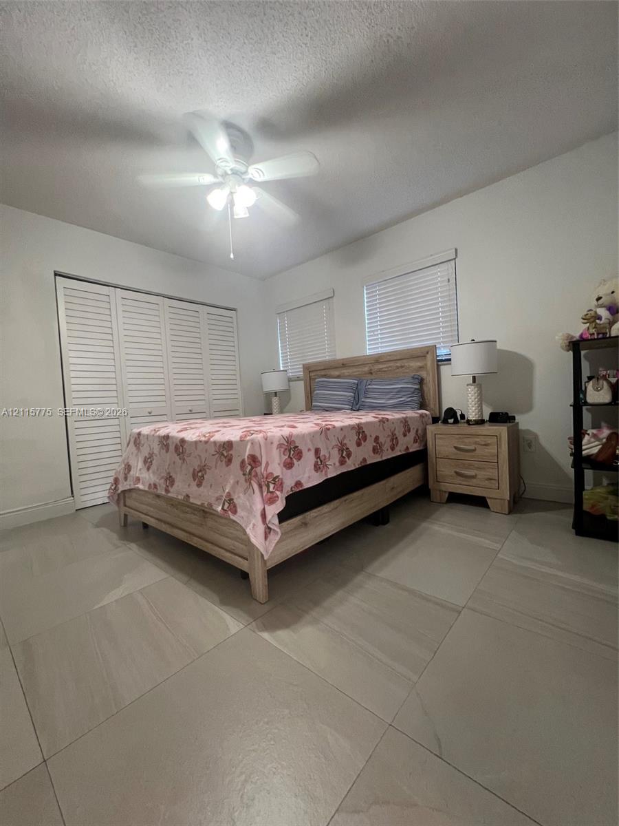 Large-format tile flooring, louvered closet doors, and a ceiling fan with integrated lighting