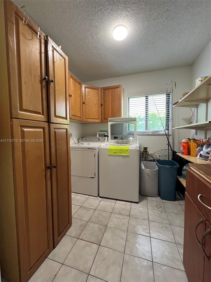 Laundry room featuring tile flooring, wood-finish cabinetry, built-in shelving, and a horizontal window