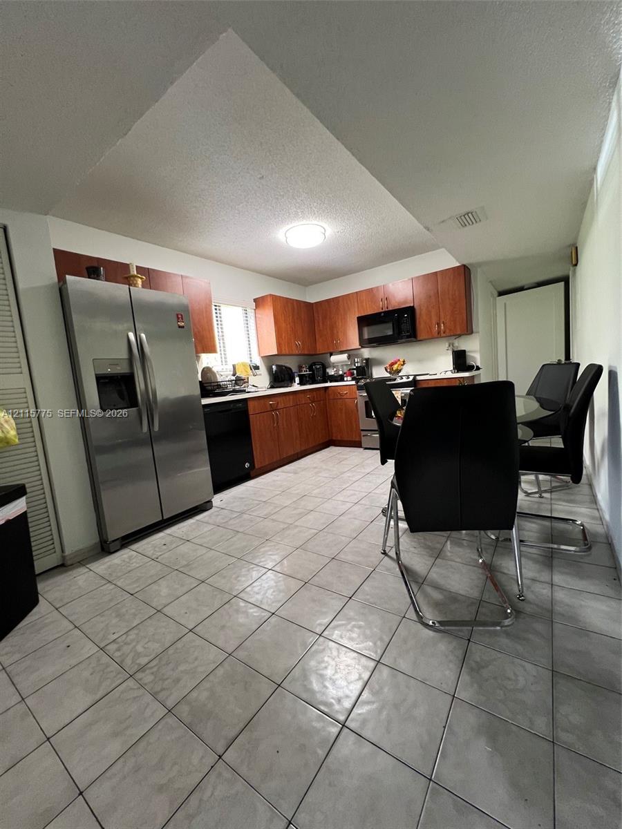 Kitchen featuring wood cabinetry, stainless steel side-by-side refrigerator, built-in microwave, and tile flooring