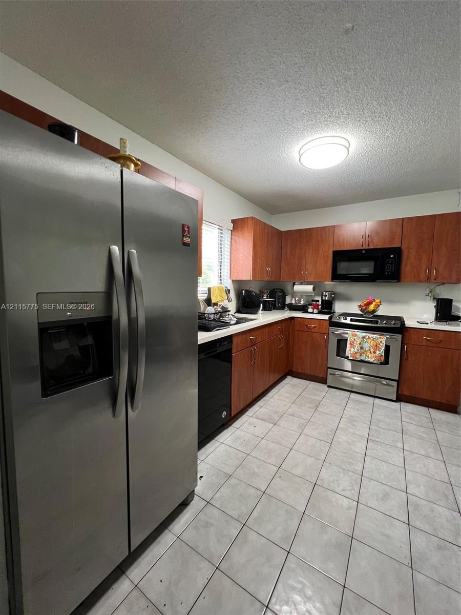 Kitchen featuring wood-finish cabinetry, stainless steel refrigerator, built-in microwave, stainless steel range, and tile flooring