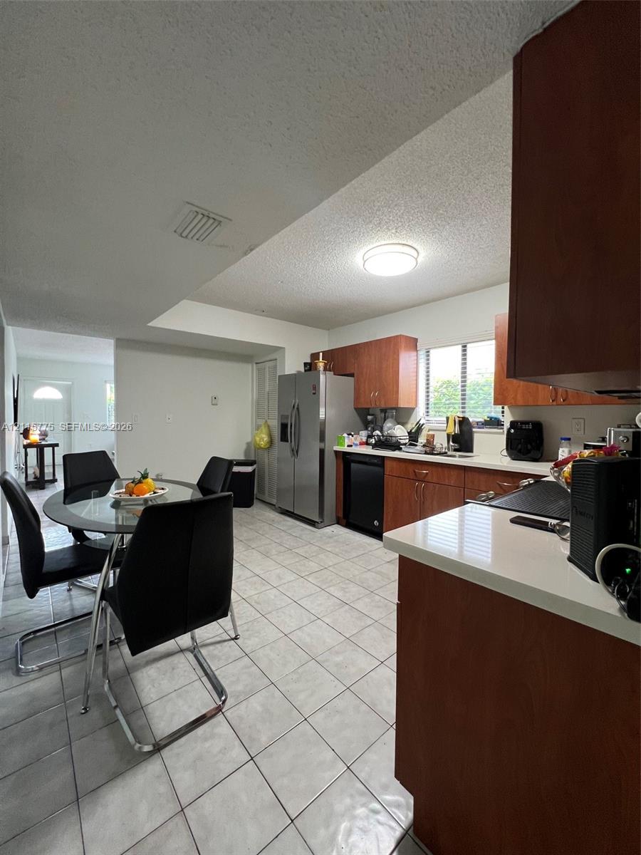 Kitchen featuring wood-finish cabinetry, solid surface countertops, stainless steel side-by-side refrigerator, under-cabinet lighting, and ceramic tile flooring