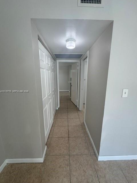 Hallway featuring neutral-toned tile flooring, recessed-panel closet doors, and a flush-mount ceiling light fixture