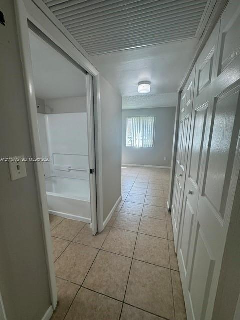Hallway featuring tile flooring, ceiling-mounted lighting, and built-in closet storage