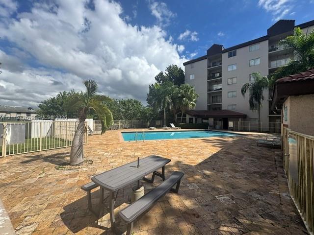 Swimming pool with metal handrails, surrounded by a natural stone paver deck, perimeter metal fencing, and mature palm trees
