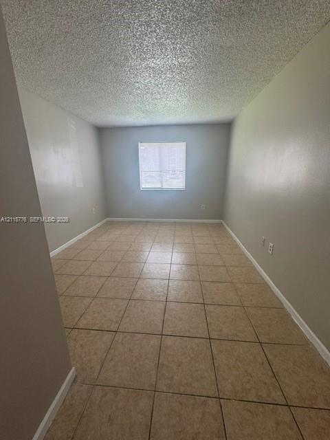 Neutral-toned interior space featuring ceramic tile flooring, textured ceiling finish, and a single centered window
