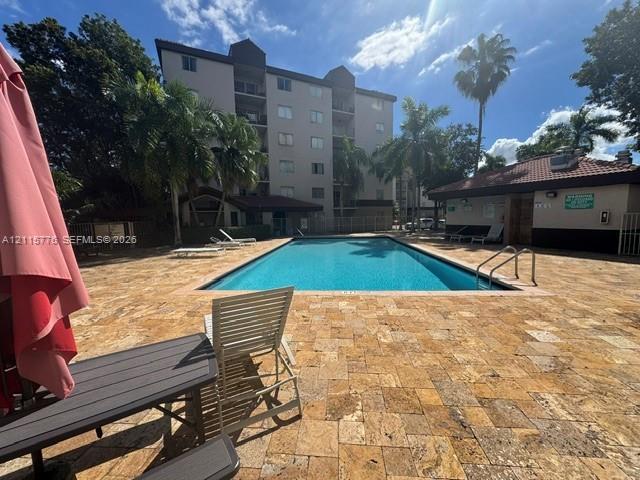 Outdoor swimming pool featuring a stone-paver deck, perimeter fencing, and mature palm trees