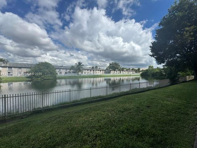 Waterfront lot featuring a manicured lawn, perimeter metal fencing, and mature trees