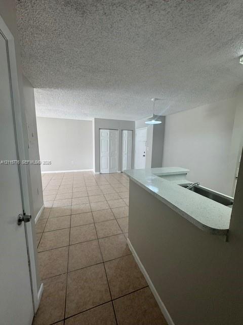 Open-concept interior featuring light-colored tile flooring, a peninsula with a stone-finish countertop, dual-panel closet doors, and a pendant light fixture