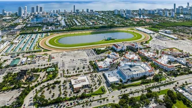 Aerial perspective featuring a racetrack, extensive parking facilities, and proximity to metropolitan buildings and coastal waters