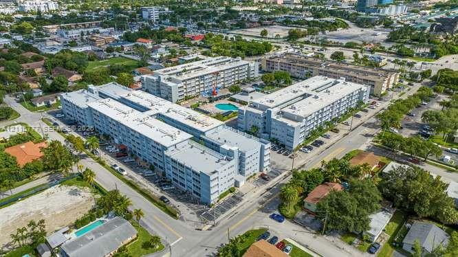 Aerial perspective of a multi-story residential complex featuring paved surface parking, a centralized swimming pool, and manicured landscaping