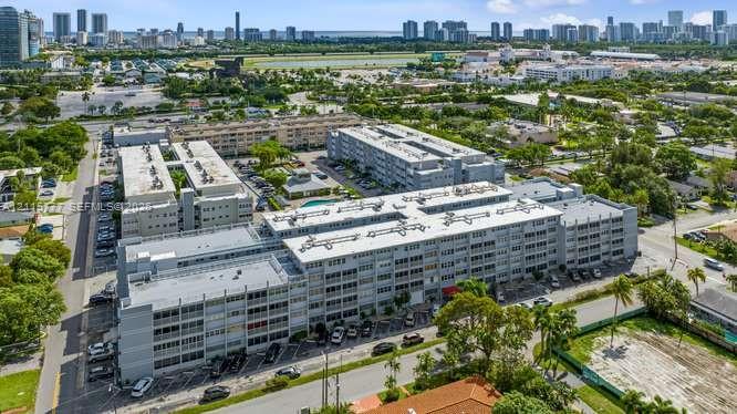 Aerial perspective of a multi-story residential complex featuring flat roof architecture, surface parking, and a central swimming pool