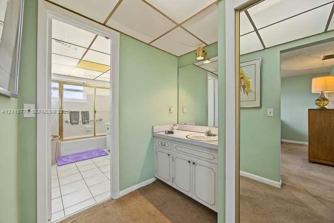 Bathroom area featuring a vanity with white cabinetry, a single sink, an integrated mirror, and a drop-in shower enclosure with a glass frame