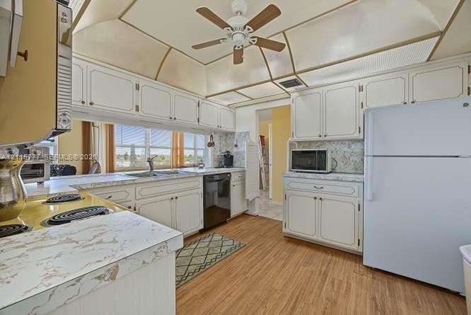 Kitchen featuring white cabinetry with decorative trim, wood-finish flooring, tray ceiling with recessed lighting, and stone-finish laminate countertops