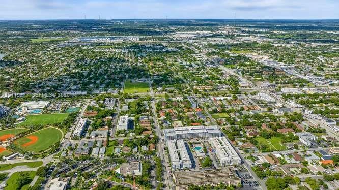 Aerial perspective of an established residential area featuring mature tree canopy, multi-family residential structures, green spaces, and recreational ball fields