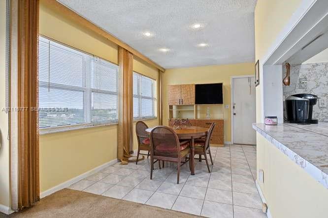 Large windows with exterior scenery, tile flooring, recessed ceiling lighting, and a kitchen pass-through with stone-finish countertop