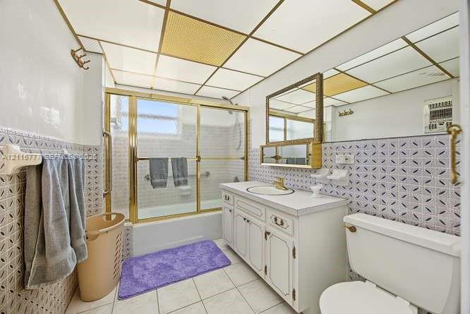 Bathroom featuring a vanity with white cabinetry, a composite countertop, and an integrated circular sink, complemented by patterned wall tile, a metal-framed shower enclosure, and a grid-style ceiling panel system