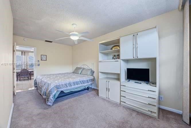 Neutral wall tones, carpeted flooring, built-in white cabinetry with integrated shelving and drawers, and a ceiling fan with light fixture