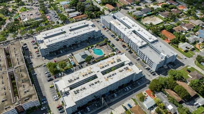 Aerial view of a residential complex featuring multiple multi-story buildings, a centralized outdoor swimming pool, and designated on-site surface parking