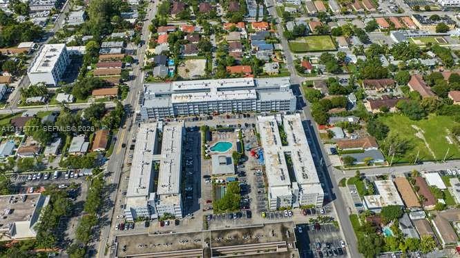 Aerial perspective of a multi-story residential complex featuring a central outdoor swimming pool, paved surface parking, flat roof architecture, and integrated landscaping