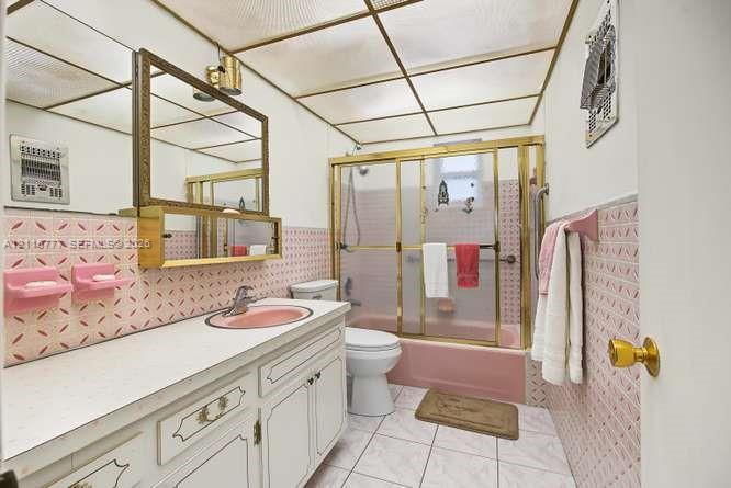 Bathroom featuring a built-in vanity with countertop sink, patterned tile wall accents, a bathtub with sliding glass doors, and a decorative grid ceiling