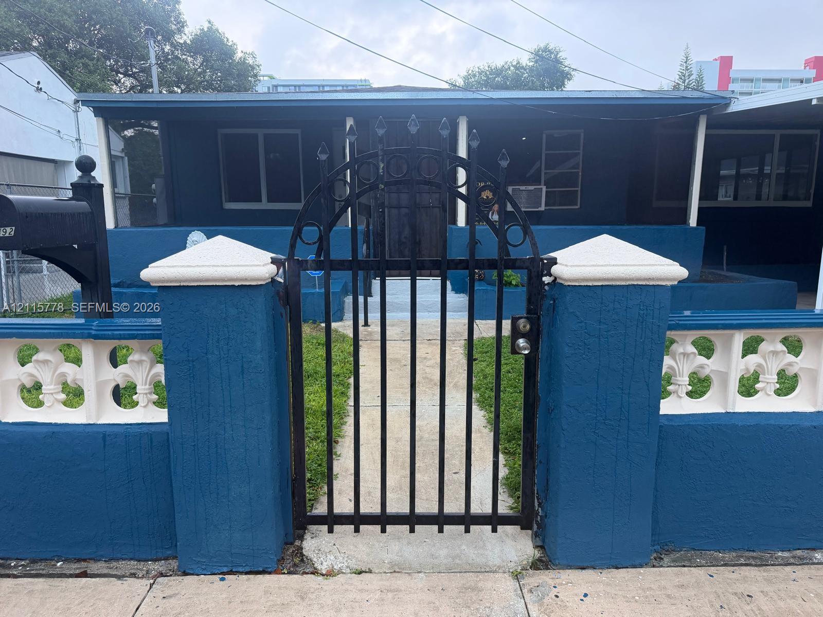 Exterior featuring a decorative wrought-iron arched gate, stone-capped stucco perimeter wall with ornamental concrete masonry units, and a covered front porch