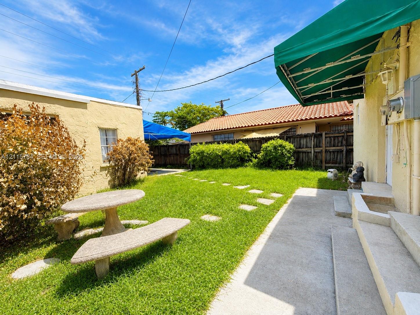 Exterior courtyard featuring a grass lawn, paved stone pathway, green retractable awning, and textured stucco walls