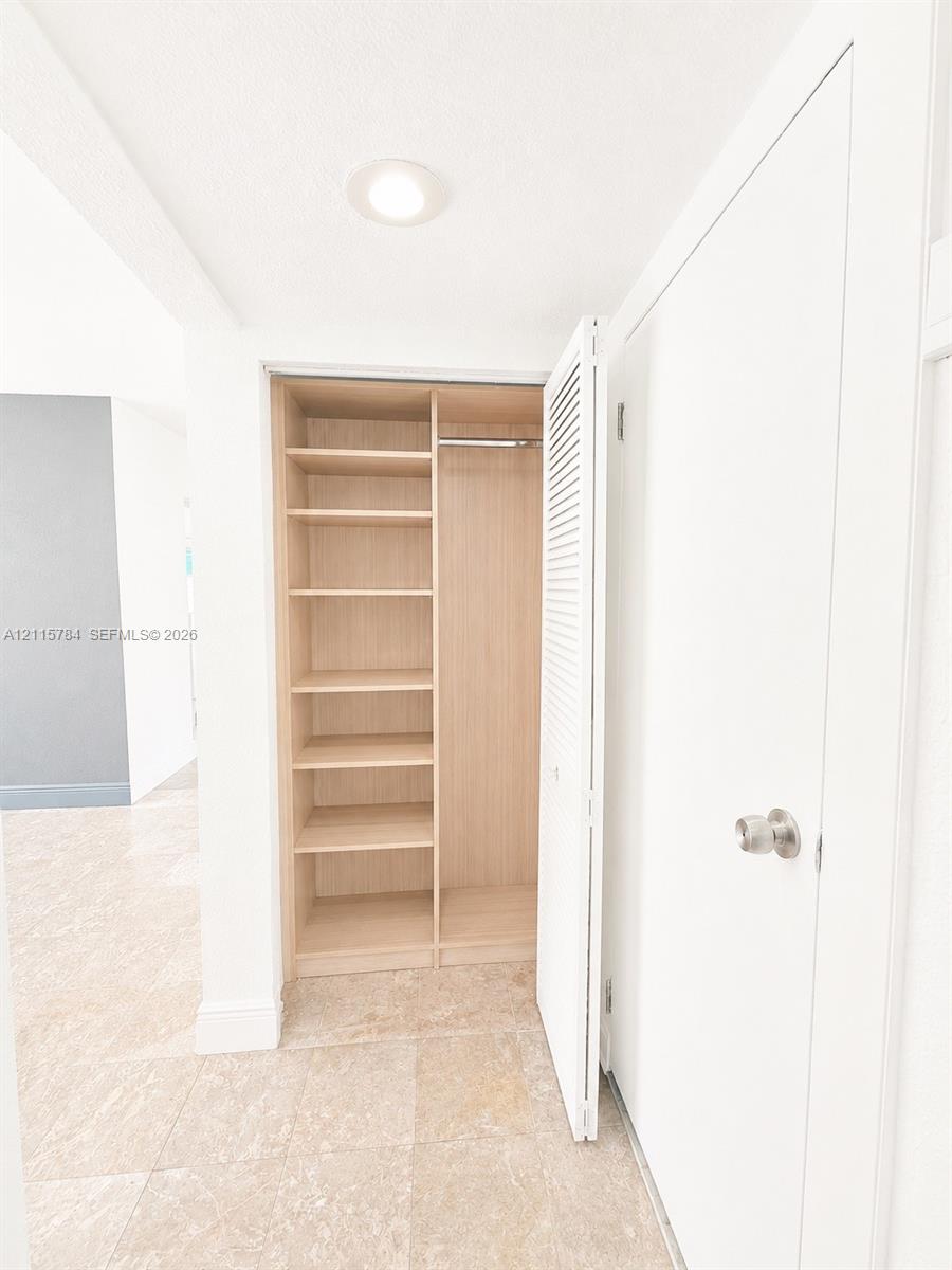 Built-in closet featuring light-toned wood shelving, a metal garment rod, and louvered folding doors, set against stone-finish flooring and recessed ceiling lighting