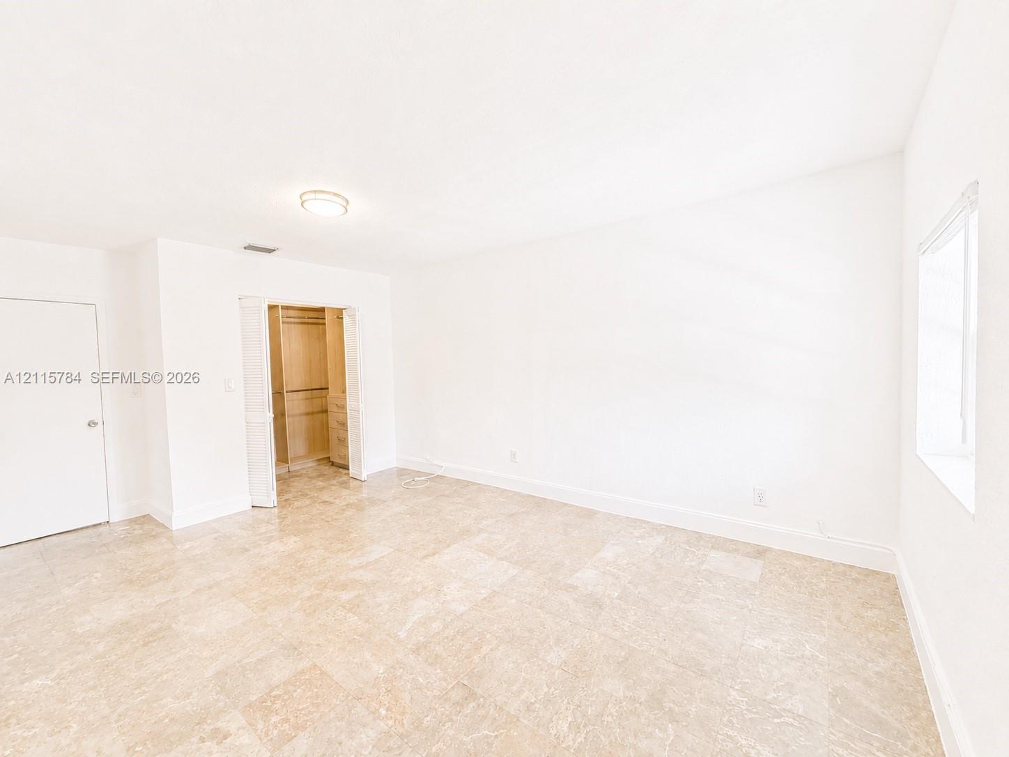 Bright interior space featuring polished tile flooring, neutral wall finishes, a window with natural light, and a built-in closet with shelving