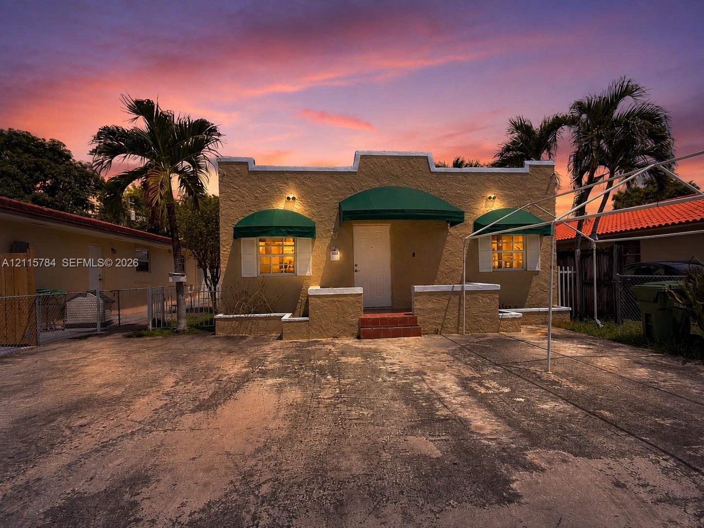Single-story residence featuring a Mission-style parapet, stucco exterior, decorative green window and entry awnings, and palm-lined landscaping Single-story residence featuring a Mission-style parapet, stucco exterior, decorative green window and entry awnings, and palm-lined landscaping