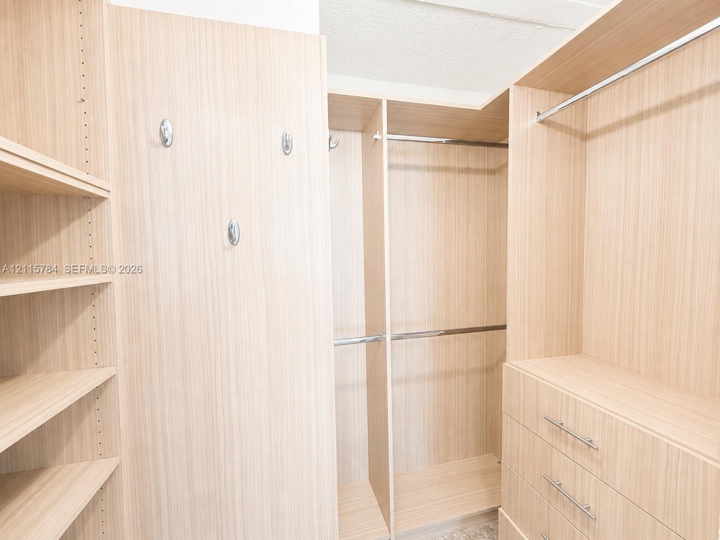 Custom reach-in closet featuring light-toned wood-finish cabinetry, built-in shelving, integrated hanging rods, three-drawer storage unit, and polished metal hardware