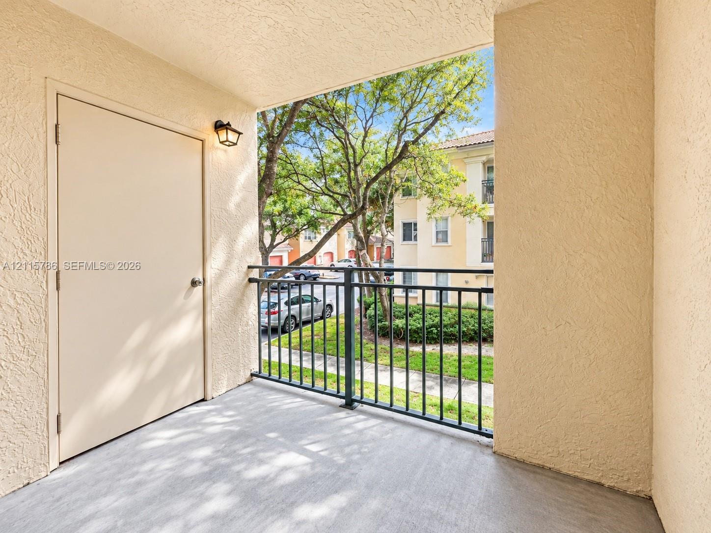 Covered balcony featuring textured exterior walls, concrete flooring, black metal railing, and an attached storage closet with exterior lighting