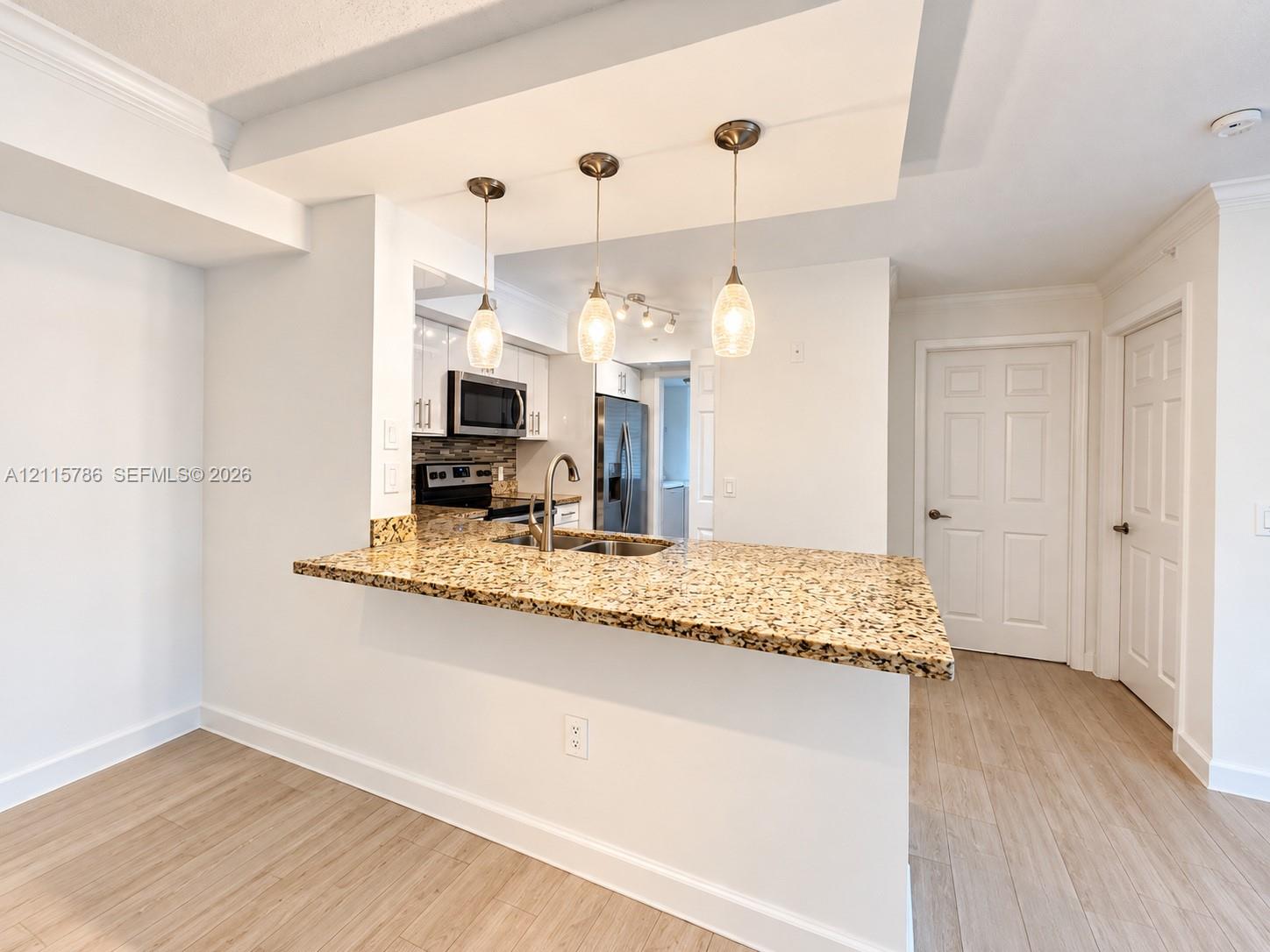 Kitchen featuring a stone-surface breakfast bar, wood-finish flooring, white shaker-style cabinetry, a stainless steel undermount sink, and three pendant light fixtures