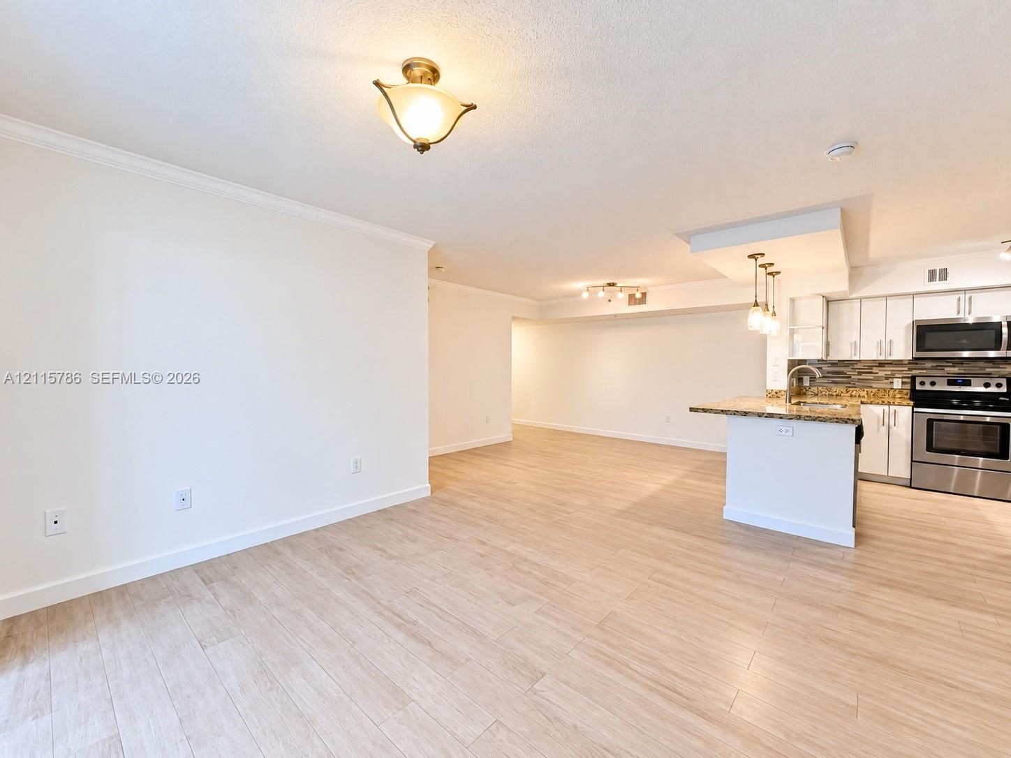 Open-concept interior featuring light wood-finish flooring, kitchen island with stone countertop, stainless steel appliances, tiled backsplash, and recessed and pendant lighting