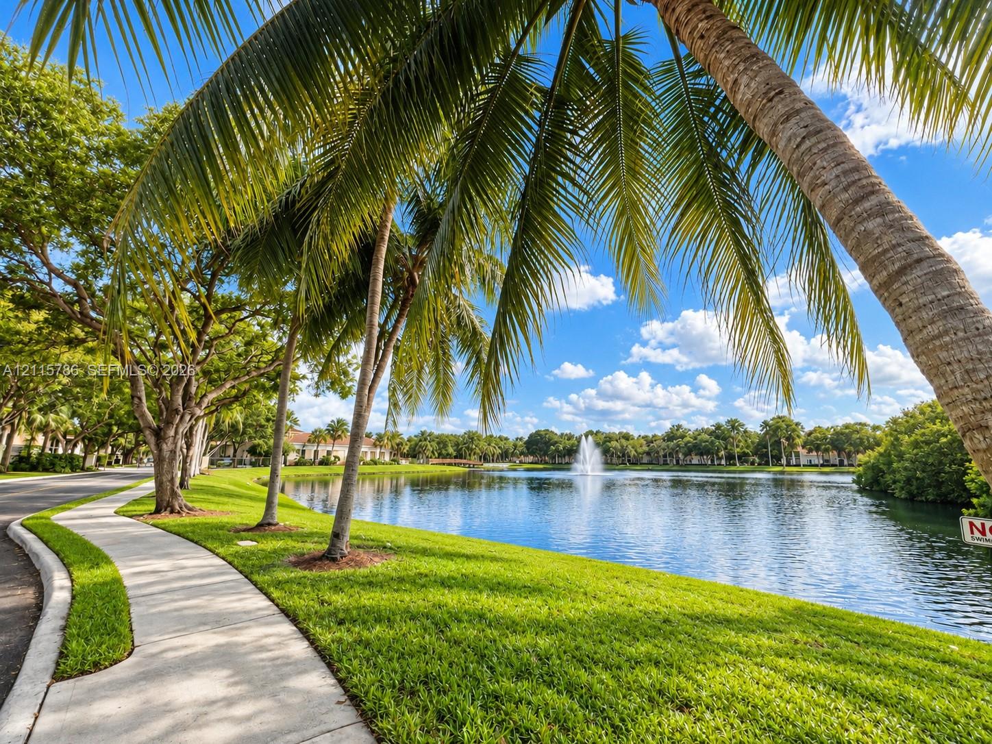 Concrete walking path, expansive waterfront, central fountain, mature palm trees, and manicured green space