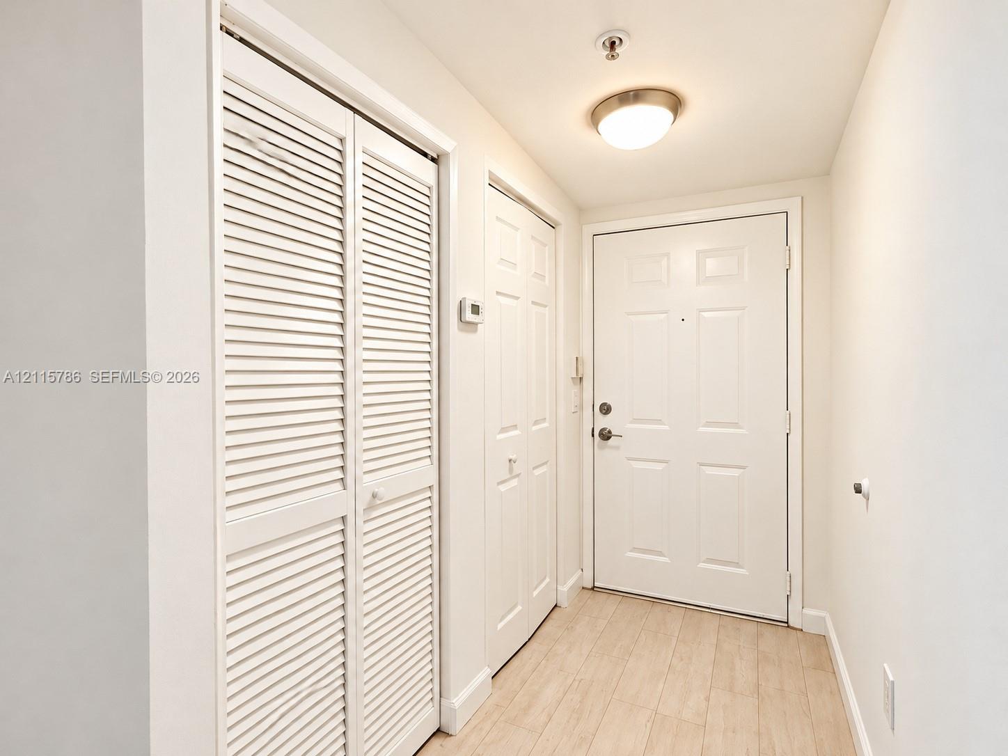 Entryway featuring light-toned wood-finish flooring, white louvered-style closet doors, a paneled solid entry door with integrated deadbolt, and a flush-mount dome light fixture