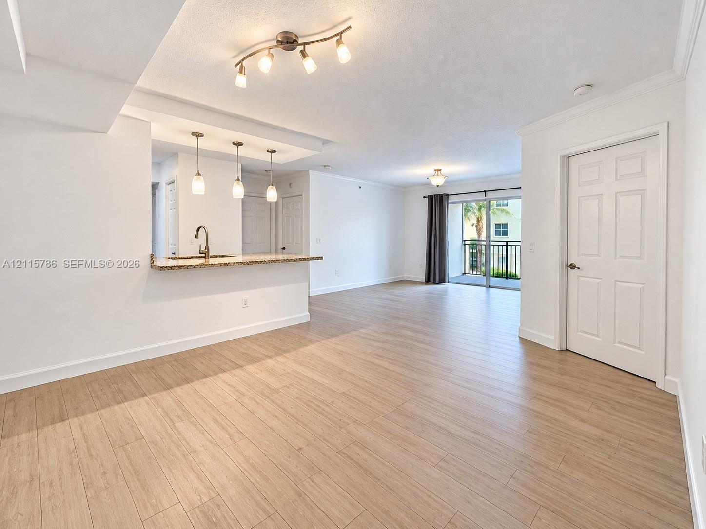 Open-concept area featuring wood-finish flooring, a kitchen pass-through with stone-surfaced breakfast bar, pendant lighting, and sliding glass doors to a private balcony