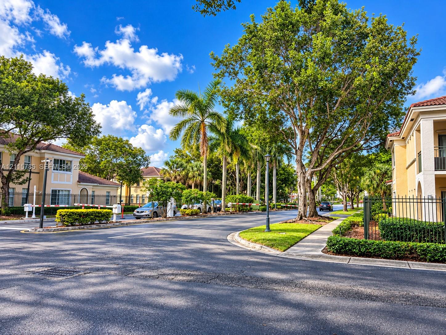 Community grounds featuring paved roadways, mature trees, manicured hedges, and decorative metal fencing