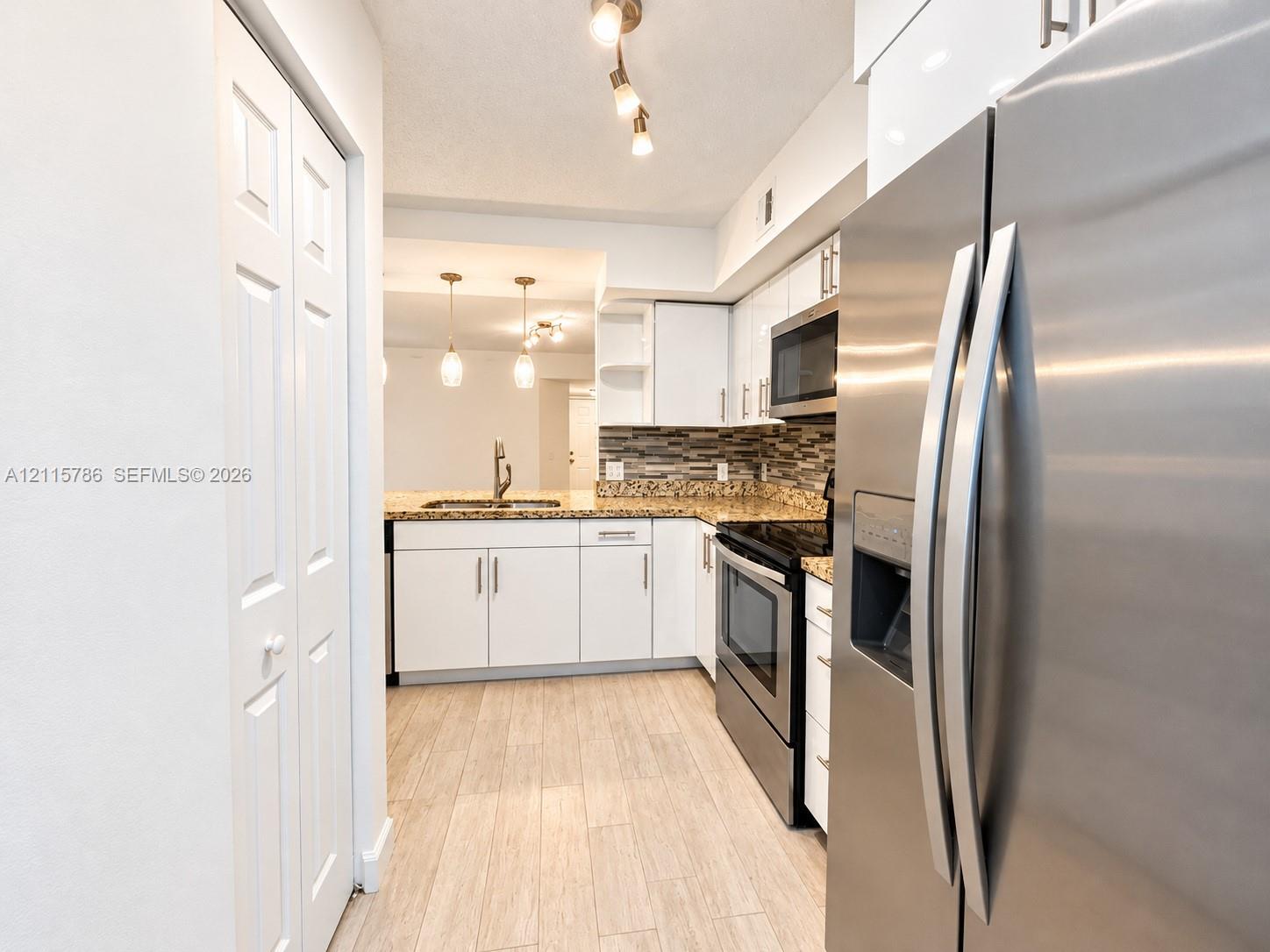 Kitchen featuring white cabinetry, stone-finish countertops, stainless steel appliances, multi-toned tile backsplash, and wood-finish flooring